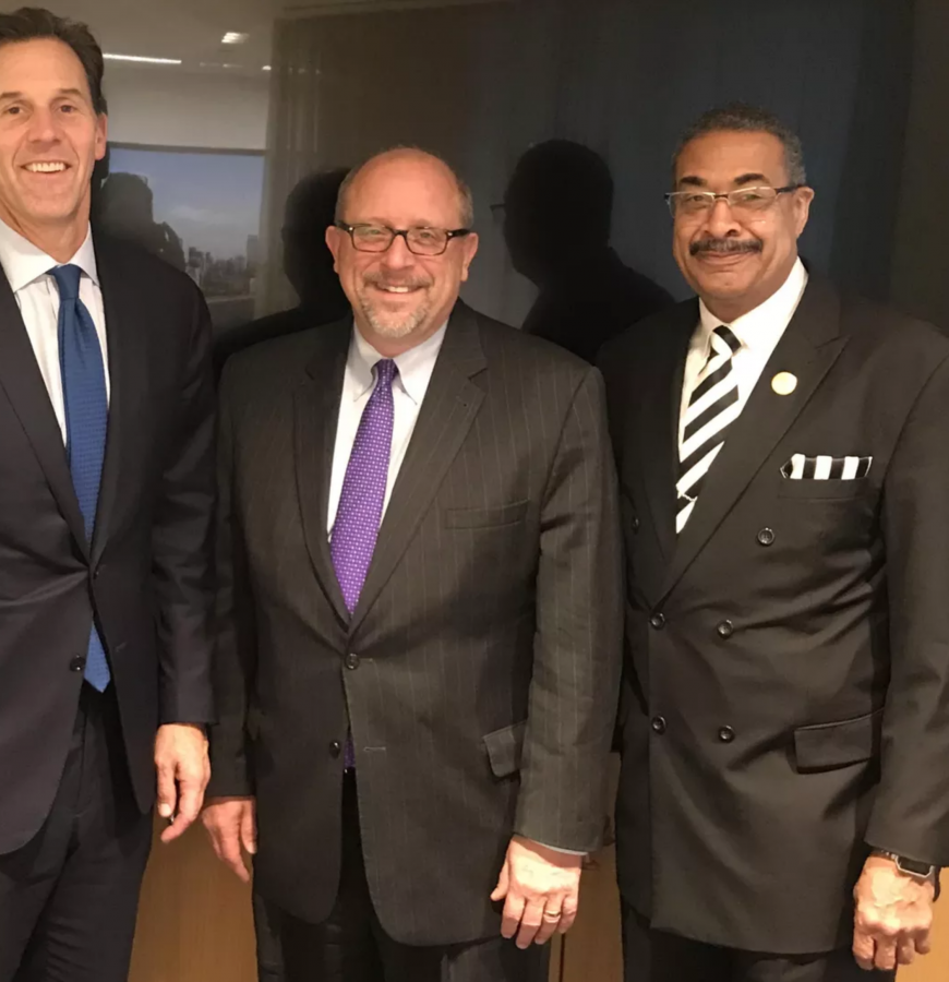 four men in suits stand shoulder to shoulder smiling